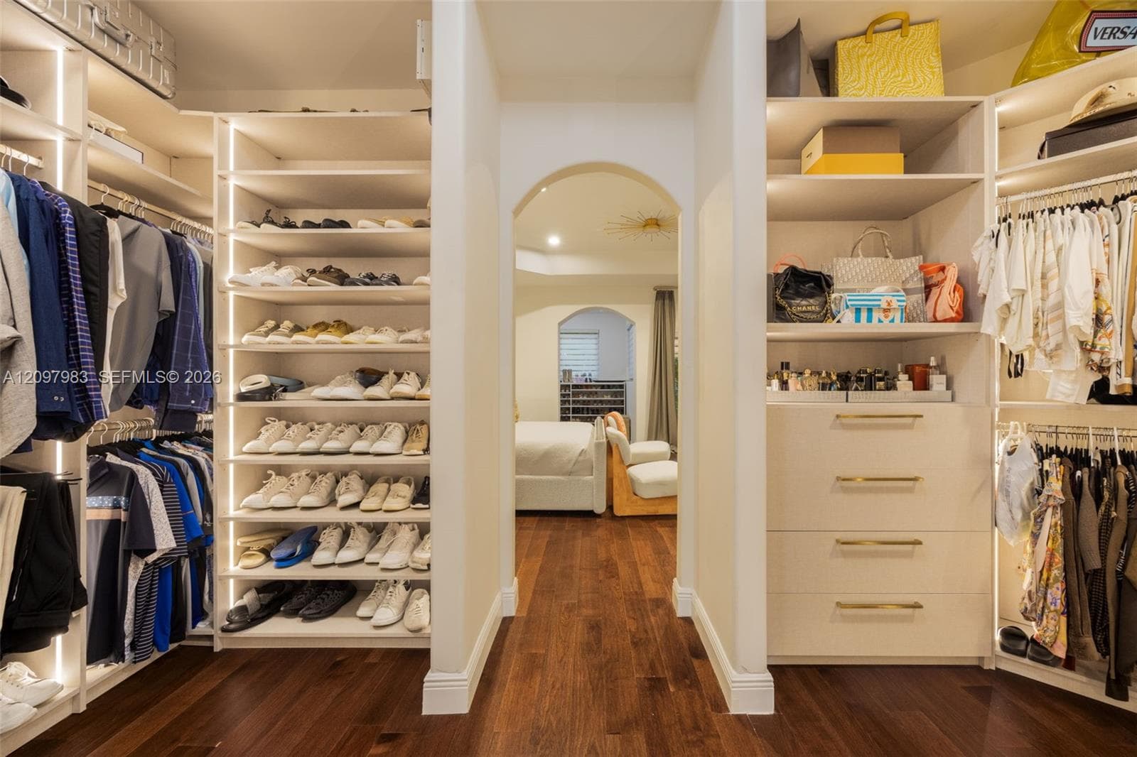 Custom walk-in closet featuring extensive built-in shelving, integrated vertical LED lighting, multiple soft-close drawers with metallic pulls, and wood-finish flooring