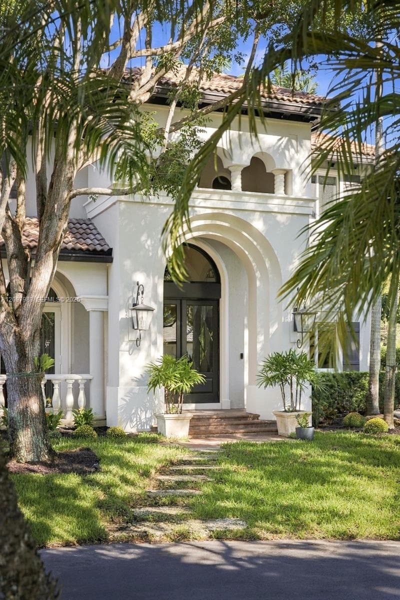 Stucco exterior featuring a prominent arched entryway, clay tile roof, decorative upper-level balustrade, and stone-finished steps