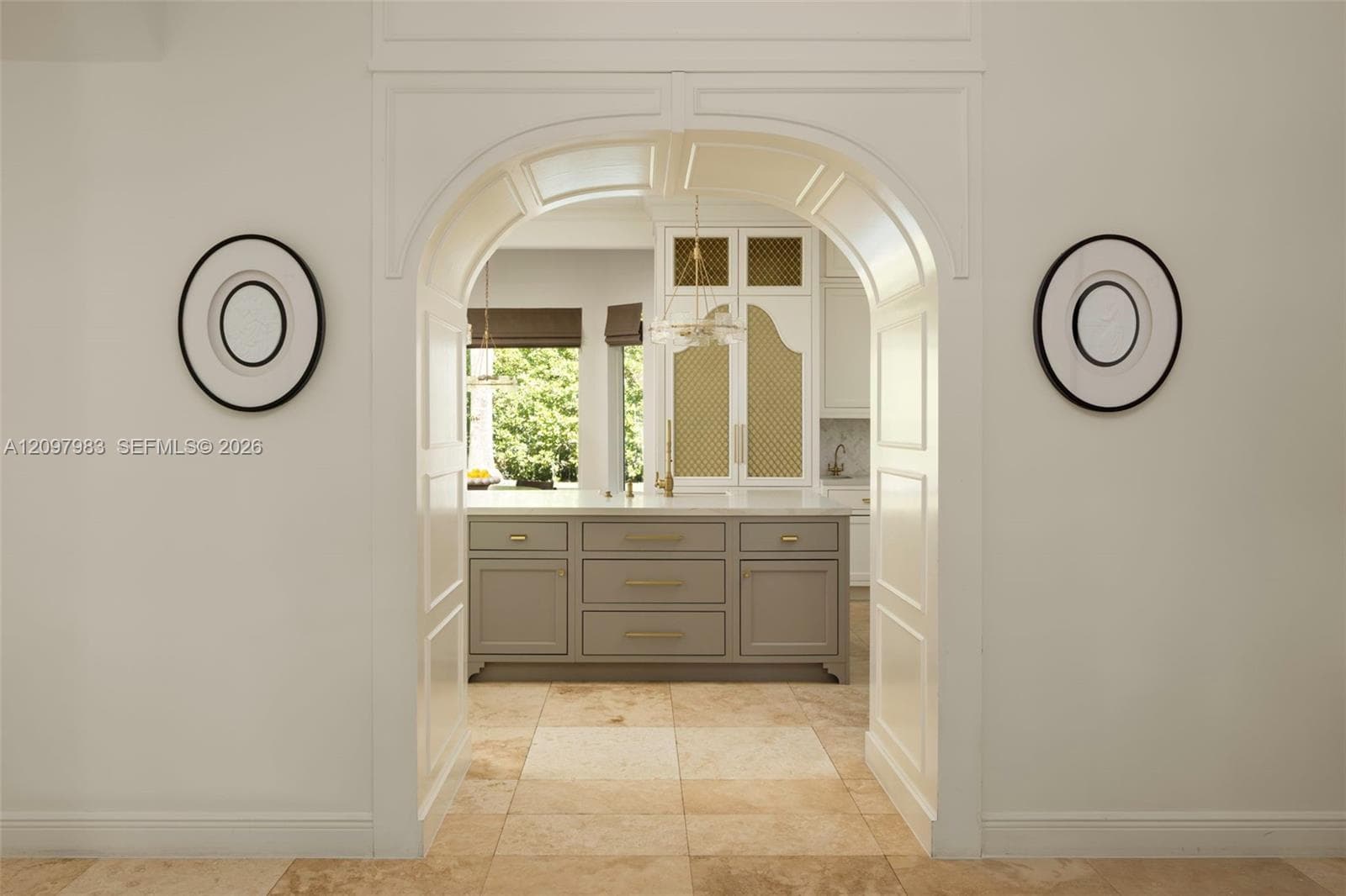 Arched entryway featuring intricate millwork, tile flooring, central kitchen island with drawers, and built-in cabinetry with decorative lattice-style detailing