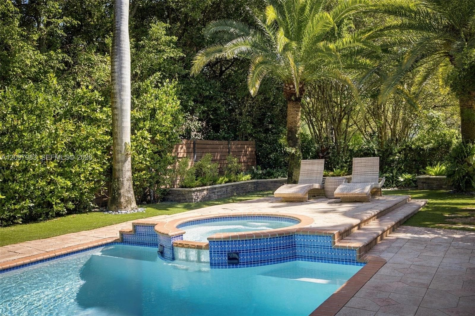 Swimming pool with an integrated raised spa, blue tile detailing, paved patio surround, and mature palm trees