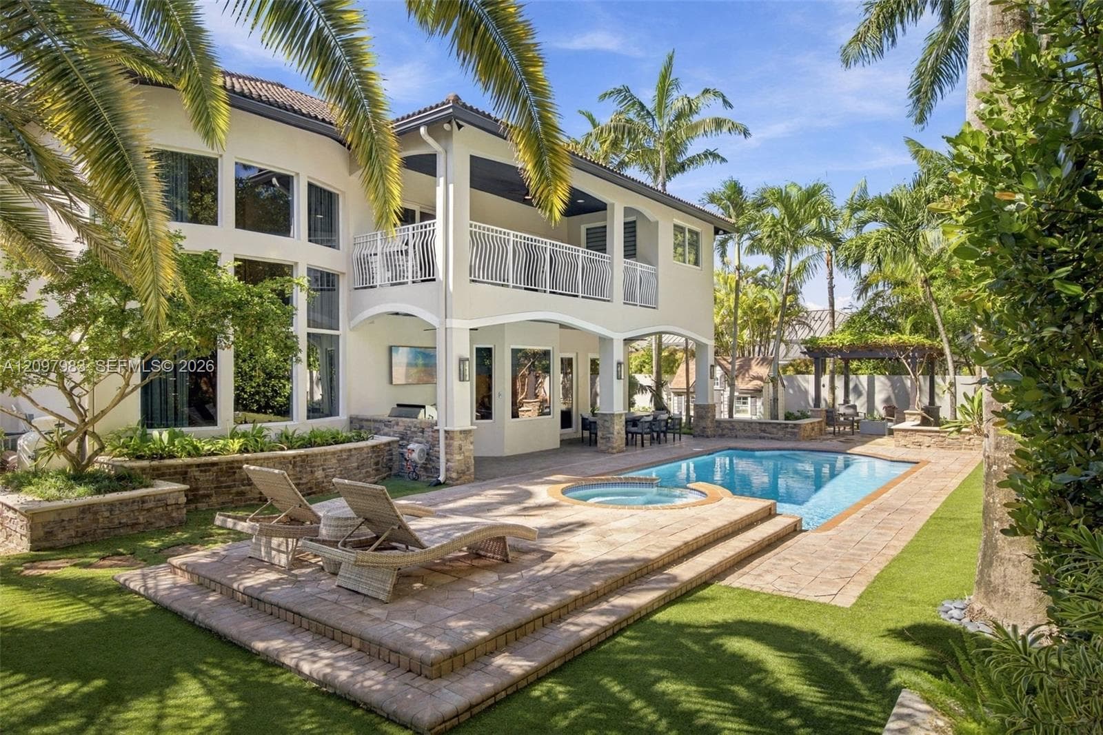 Two-story exterior featuring stone accents, a covered upper-level balcony, a multi-tiered stone paver deck, and an in-ground swimming pool with an integrated spa