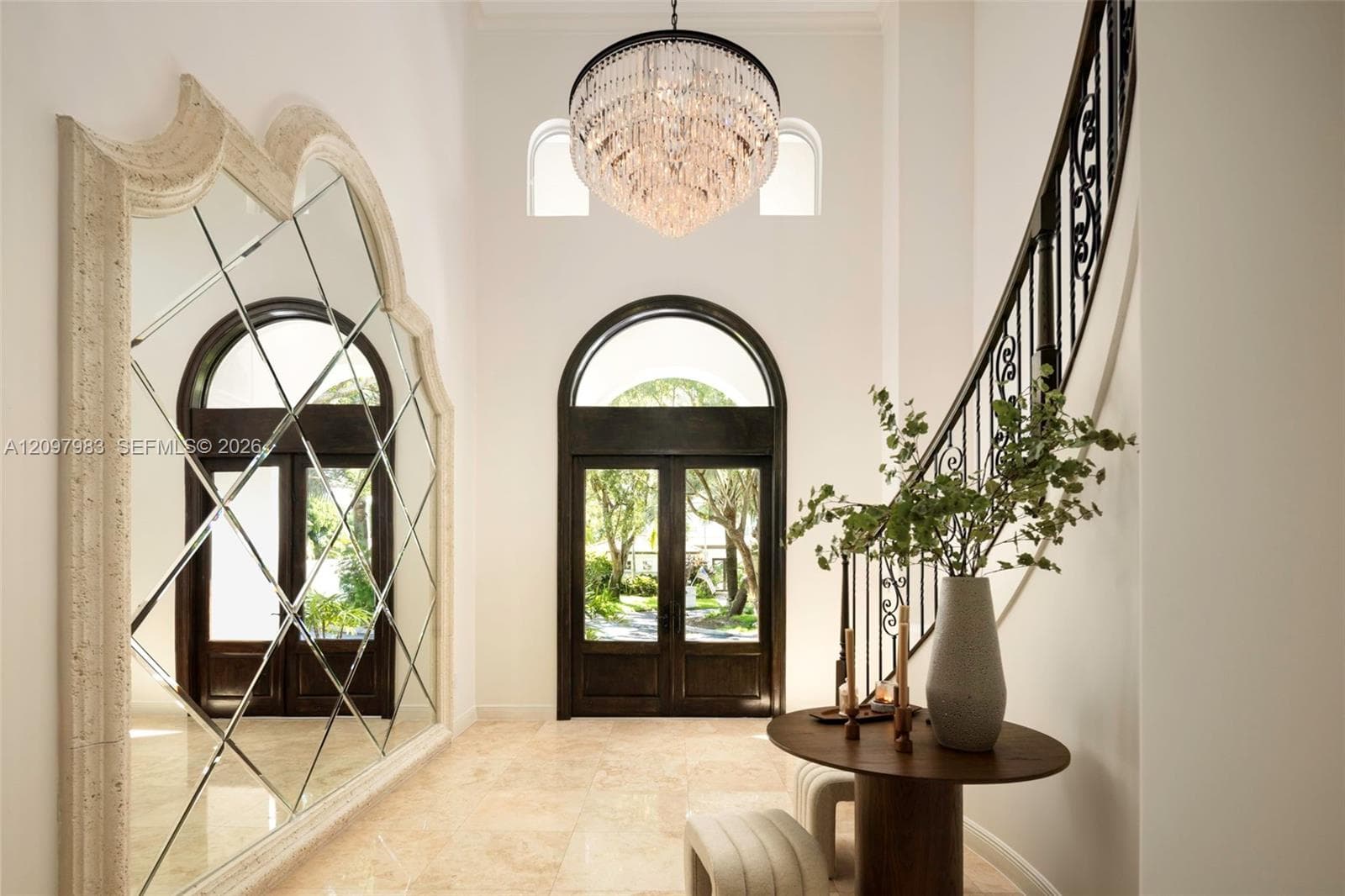 Foyer featuring a grand crystal chandelier, arched double entry doors, a large-scale decorative mirror with a stone-finish frame, stone flooring, and a curved staircase with ornate iron railing