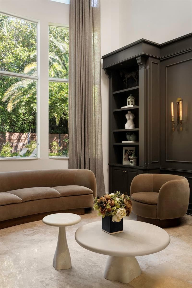 Floor-to-ceiling windows, built-in custom cabinetry with dark finish, wall-mounted brass lighting, and stone flooring