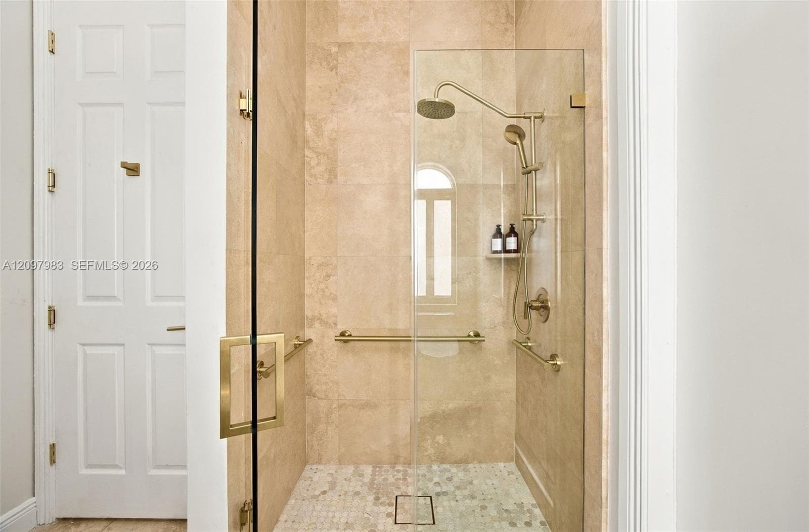 Walk-in shower featuring floor-to-ceiling stone tile, a glass enclosure, brass-finish fixtures, a dual-head shower system, and integrated brass-finish support bars