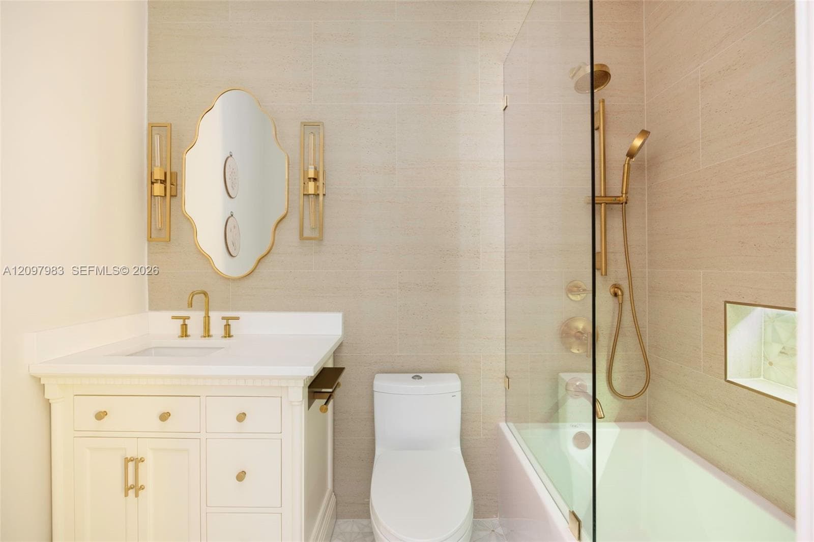 Bathroom featuring a white cabinetry vanity with a solid surface countertop, brass-finish fixtures, a frameless glass shower panel, and neutral wall tiling with an integrated shower niche