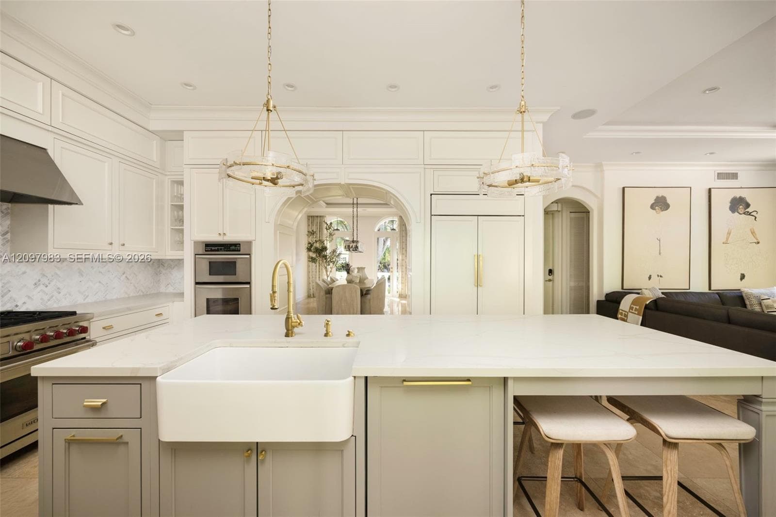 Kitchen featuring custom cabinetry, a large center island with a farmhouse sink, stone countertops, herringbone-patterned backsplash, and dual pendant lighting