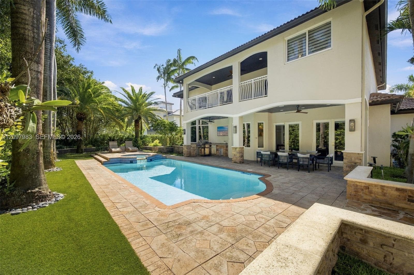 Stucco exterior featuring a two-story covered patio, custom swimming pool with integrated spa, paver hardscaping, and built-in outdoor kitchen