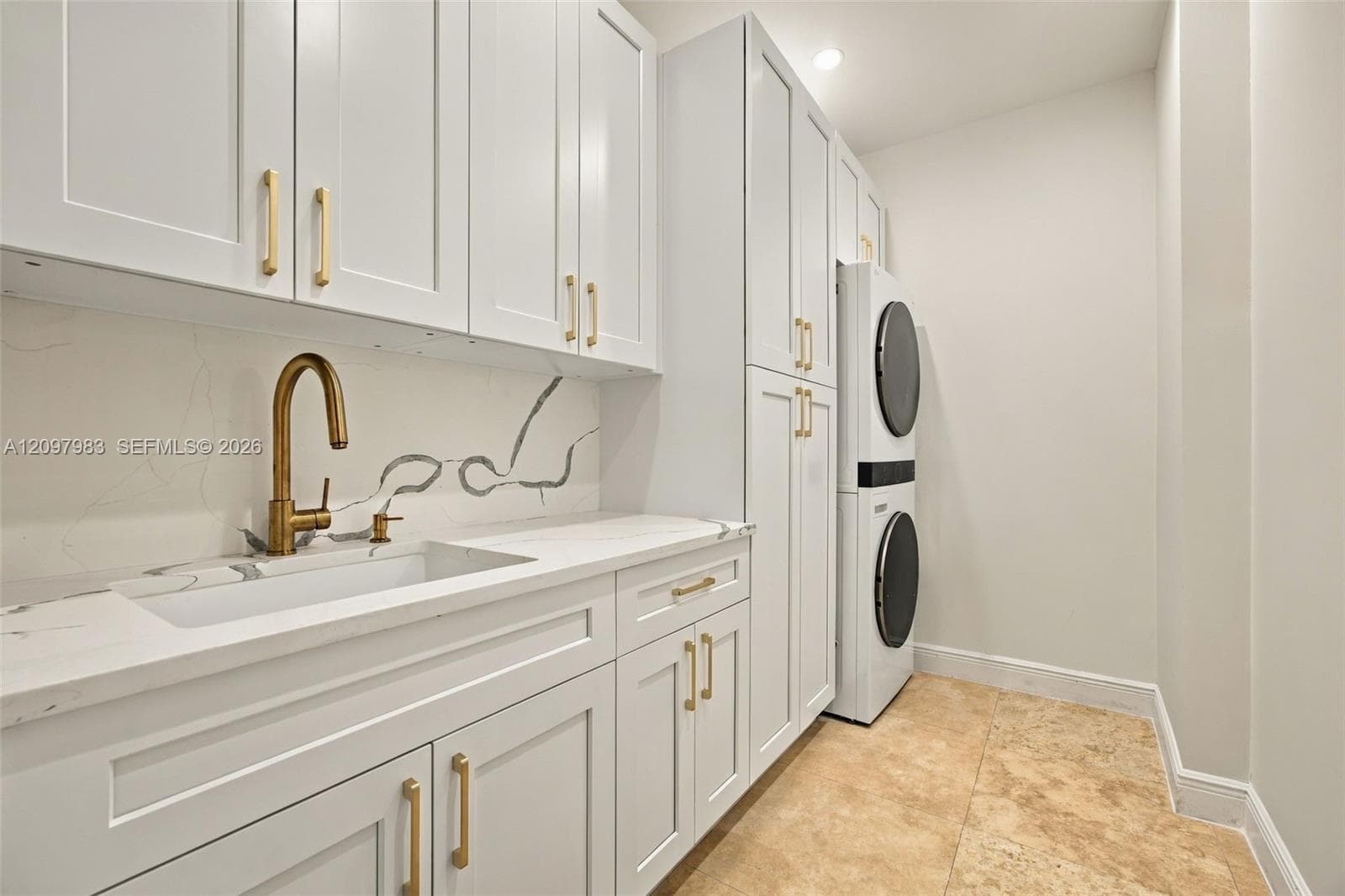 White cabinetry featuring brushed gold hardware, stone-finish countertops, integrated stone backsplash, drop-in sink with a gold-tone faucet, and tile flooring