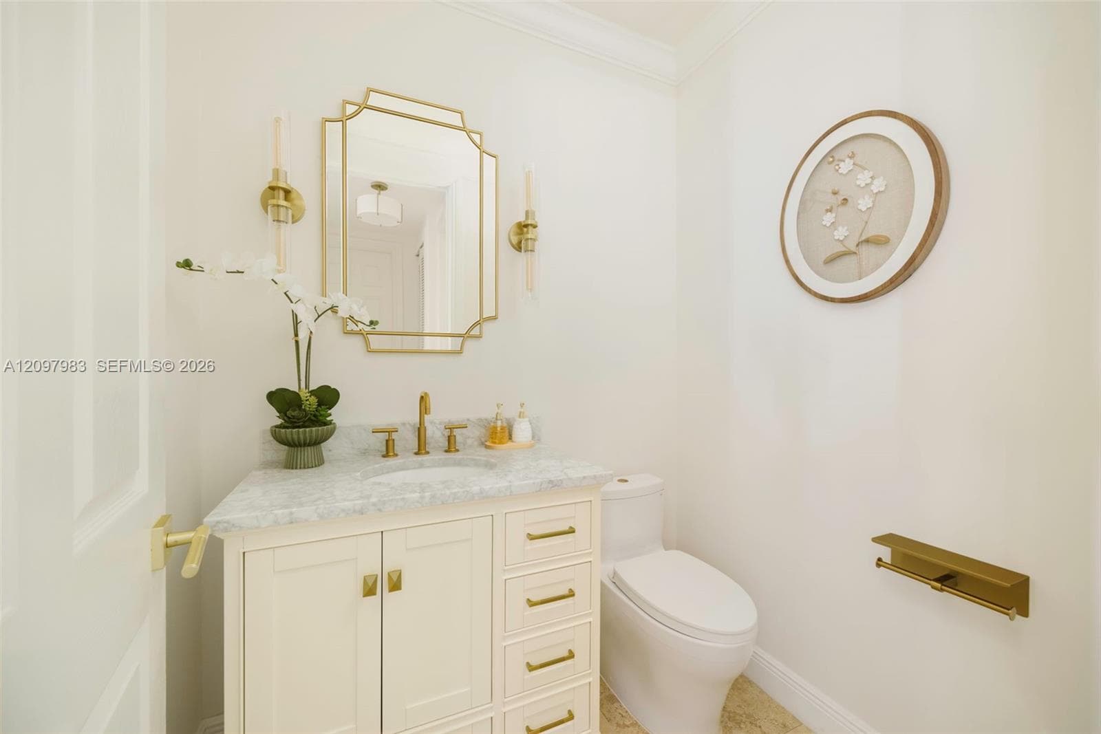 Custom cabinetry vanity with stone countertop, brass-finish fixtures, geometric wall mirror, and coordinating brass-finish hardware