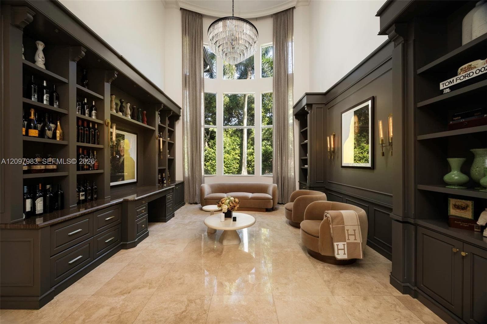 Double-height ceiling with floor-to-ceiling multi-pane windows, expansive built-in cabinetry with integrated shelving, polished stone tile flooring, and tiered crystal chandelier