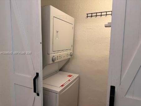 Laundry alcove featuring white sliding barn doors with matte black hardware, stacked laundry unit, and wall-mounted storage rack