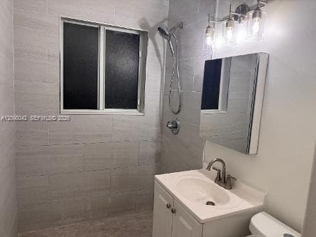 Bathroom featuring large-format light gray wall tile, a white vanity with an integrated sink, a multi-bulb vanity light fixture, and a wall-mounted shower head