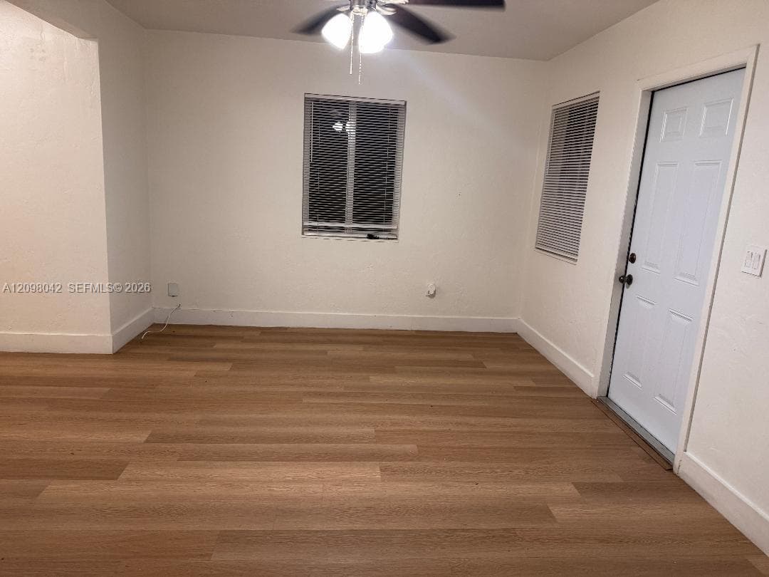 Neutral-toned interior featuring wood-finish flooring, white walls, a ceiling fan with integrated lighting, and a six-panel exterior door