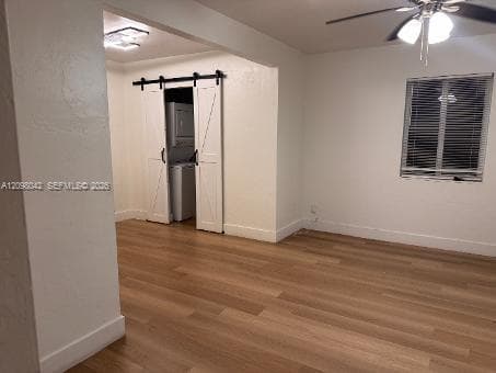 Interior space featuring wood-finish flooring, white sliding barn-style doors, and a ceiling-mounted light fixture with a fan