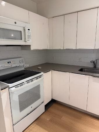 Kitchen featuring white cabinetry, solid-surface countertops, subway tile backsplash, white electric range with built-in microwave, and wood-finish flooring