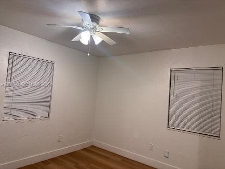 Interior space featuring wood-finish flooring, white walls, two windows with horizontal blinds, and a central ceiling fan with integrated lighting
