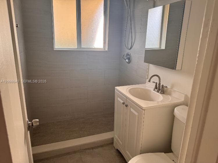 Bathroom featuring a walk-in shower with light-toned tile surround, a single-basin vanity with Shaker-style cabinet doors, a chrome faucet, and a wall-mounted medicine cabinet