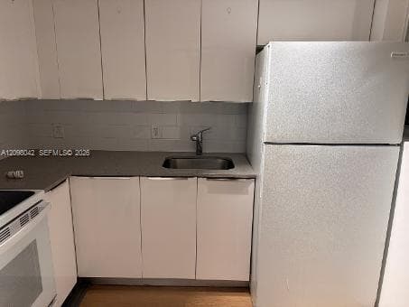 White cabinetry, stainless steel sink with metal faucet, solid-surface countertop, white subway-style backsplash, and full-size refrigerator