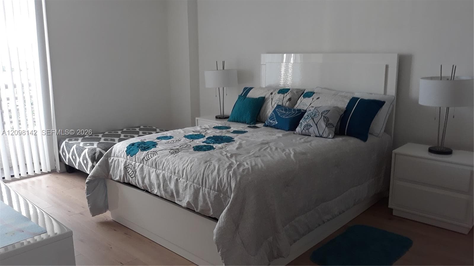 Neutral-toned bedroom featuring wood-finish flooring and vertical window blinds