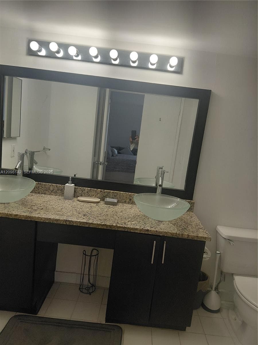 Dual-sink vanity featuring frosted glass vessel basins, stone-finish countertop, dark cabinetry, and an oversized rectangular mirror with integrated light bar