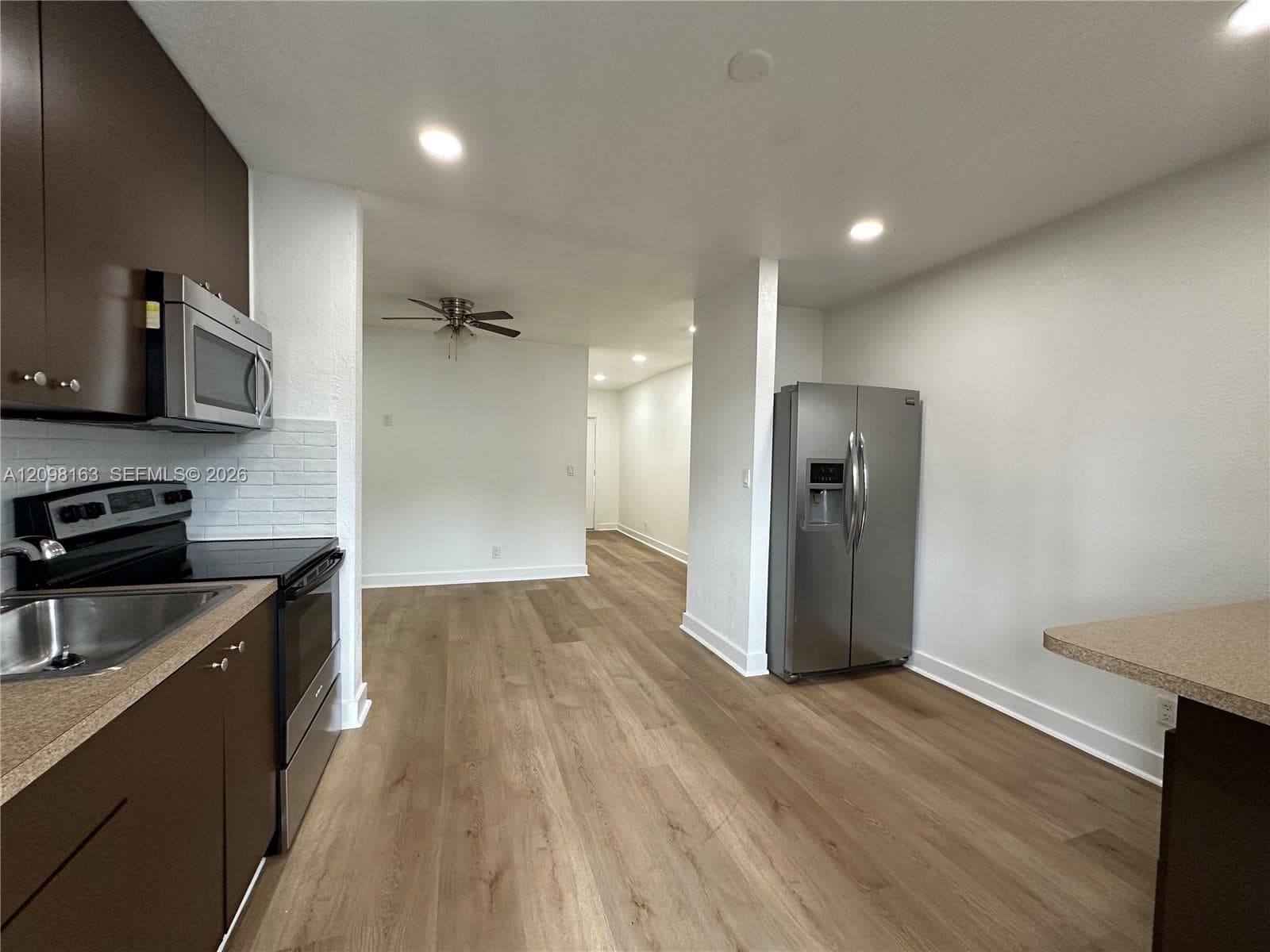 Kitchen featuring flat-panel dark cabinetry, stainless steel appliances, white brick-pattern backsplash, recessed lighting, and wood-finish flooring