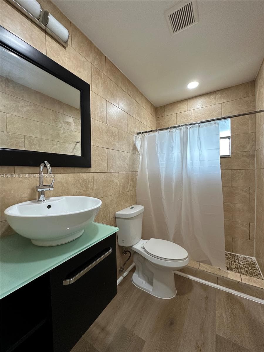 Bathroom featuring a vessel sink with a polished chrome faucet, a glass-top vanity, wall-to-wall ceramic tile, and a walk-in shower with mosaic tile flooring