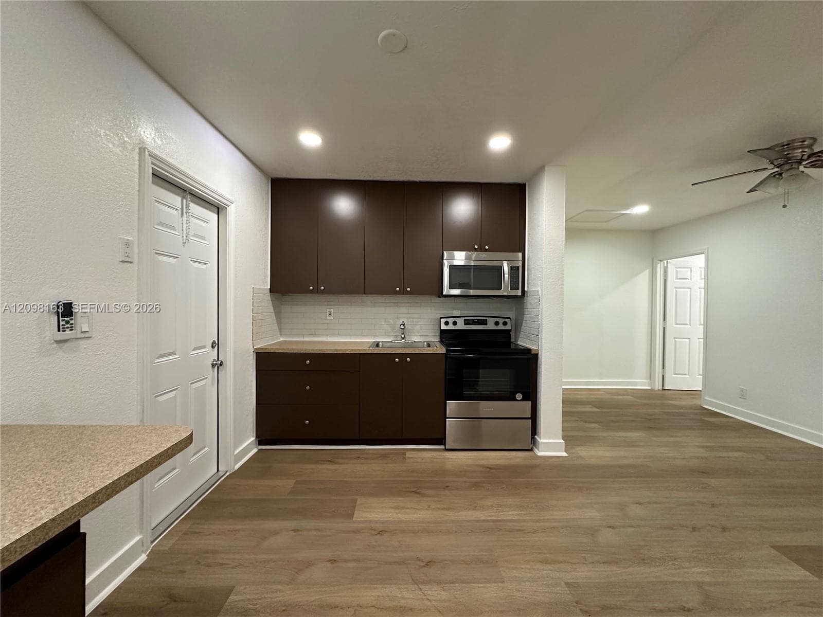 Kitchenette featuring dark-finish cabinetry, stainless steel appliances, tile backsplash, wood-finish flooring, and recessed lighting