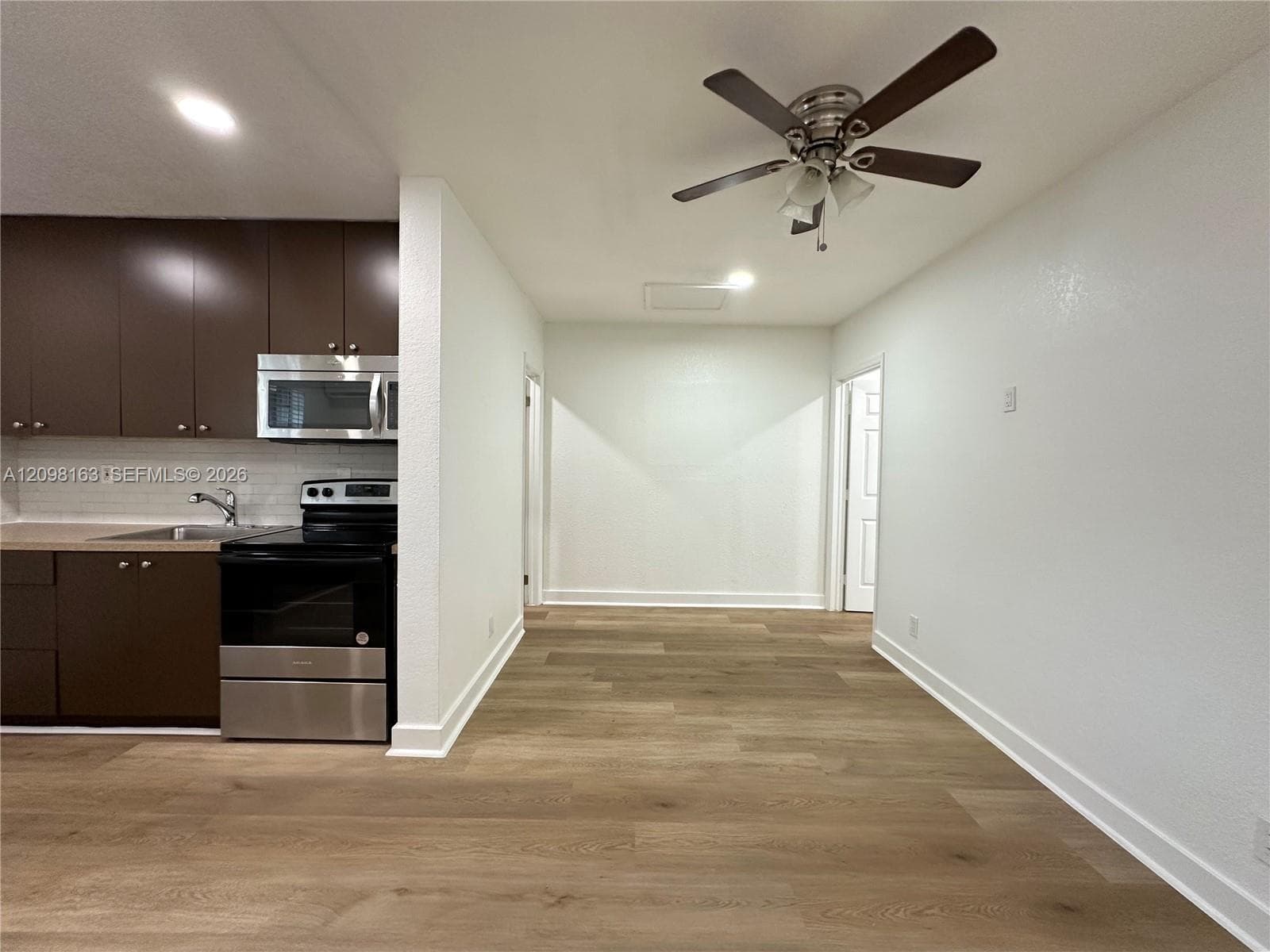 Kitchen featuring flat-panel cabinetry, stainless steel microwave and oven, wood-finish flooring, and a ceiling fan with integrated lighting