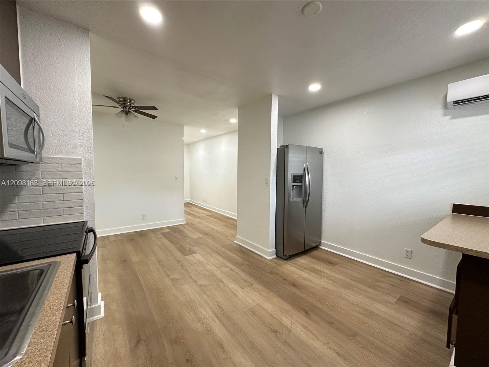 Kitchen featuring wood-finish flooring, stainless steel side-by-side refrigerator, recessed lighting, wall-mounted mini-split HVAC unit, and textured brick-pattern backsplash