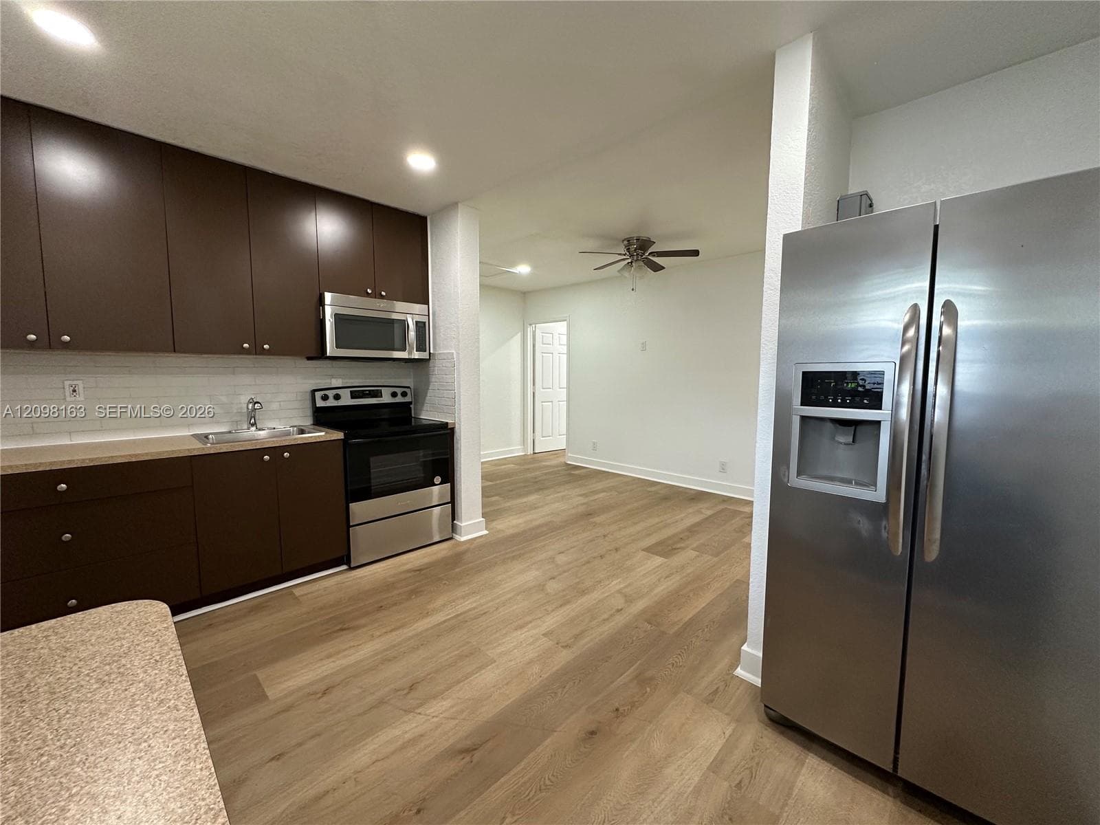 Kitchen featuring dark cabinetry, stainless steel appliances, white subway tile backsplash, solid-surface countertops, and wood-finish flooring
