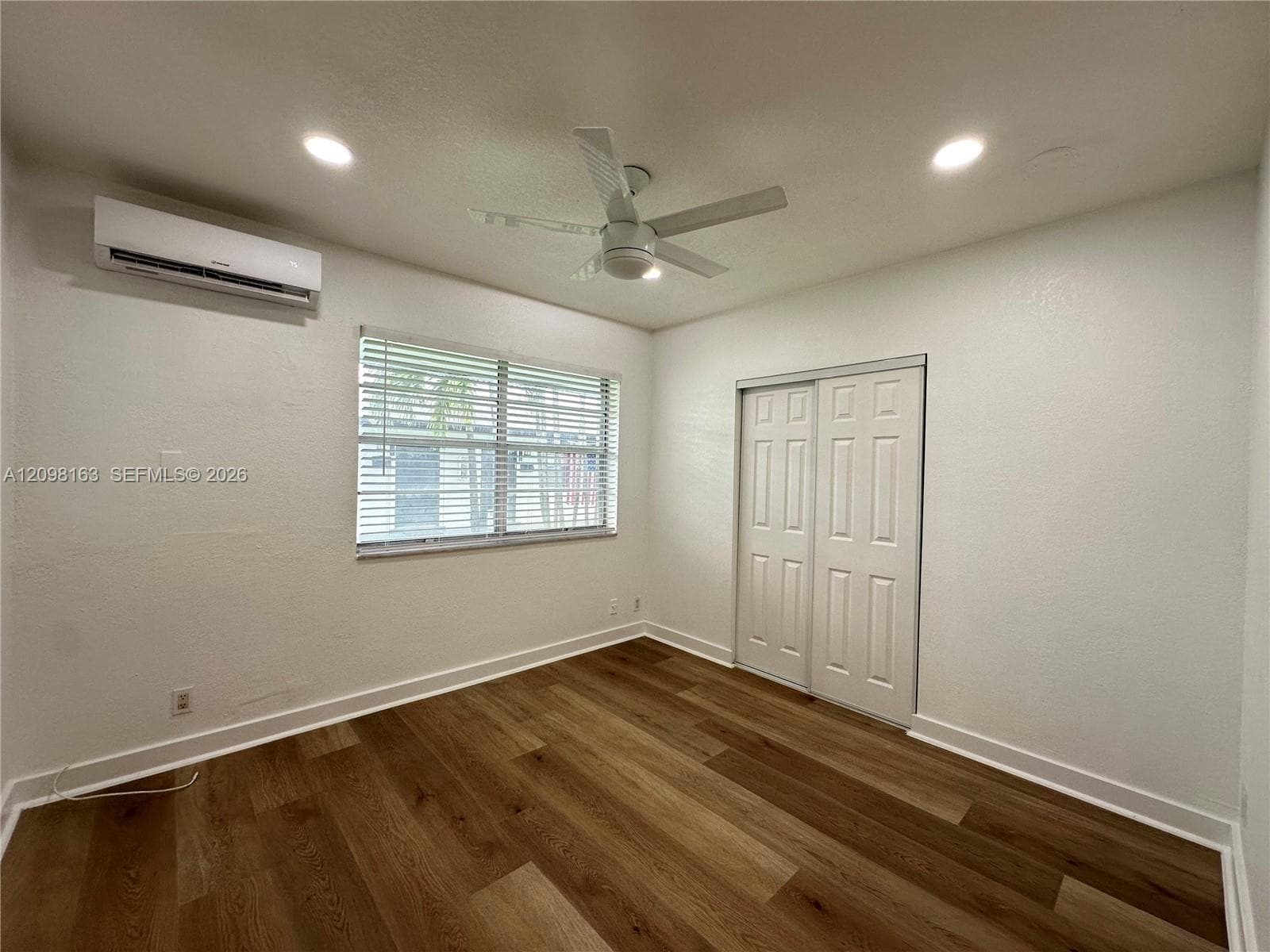 Room featuring wood-finish flooring, recessed lighting, a ceiling fan, a wall-mounted ductless air conditioning unit, and a double-door closet