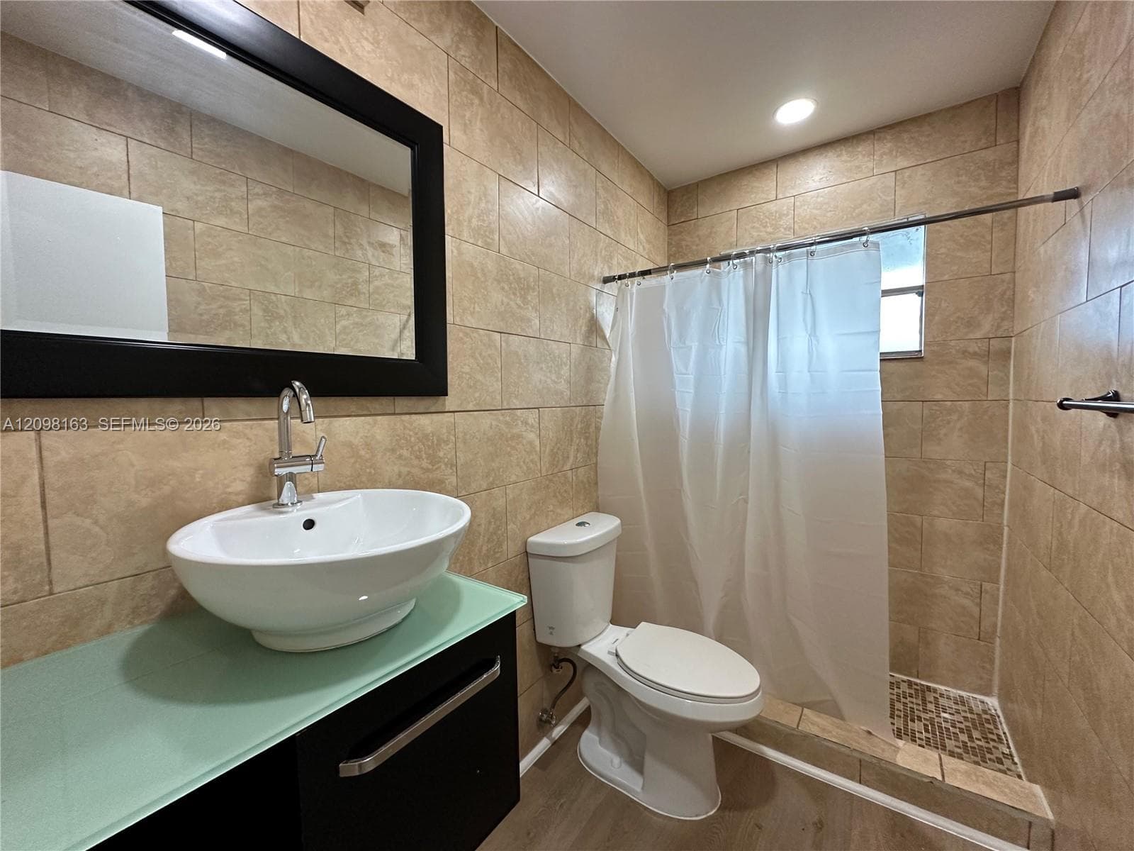 Full-bathroom featuring a vessel sink with a chrome gooseneck faucet, a glass-topped vanity cabinet, floor-to-ceiling tile walls, and a walk-in shower with stone mosaic tile flooring
