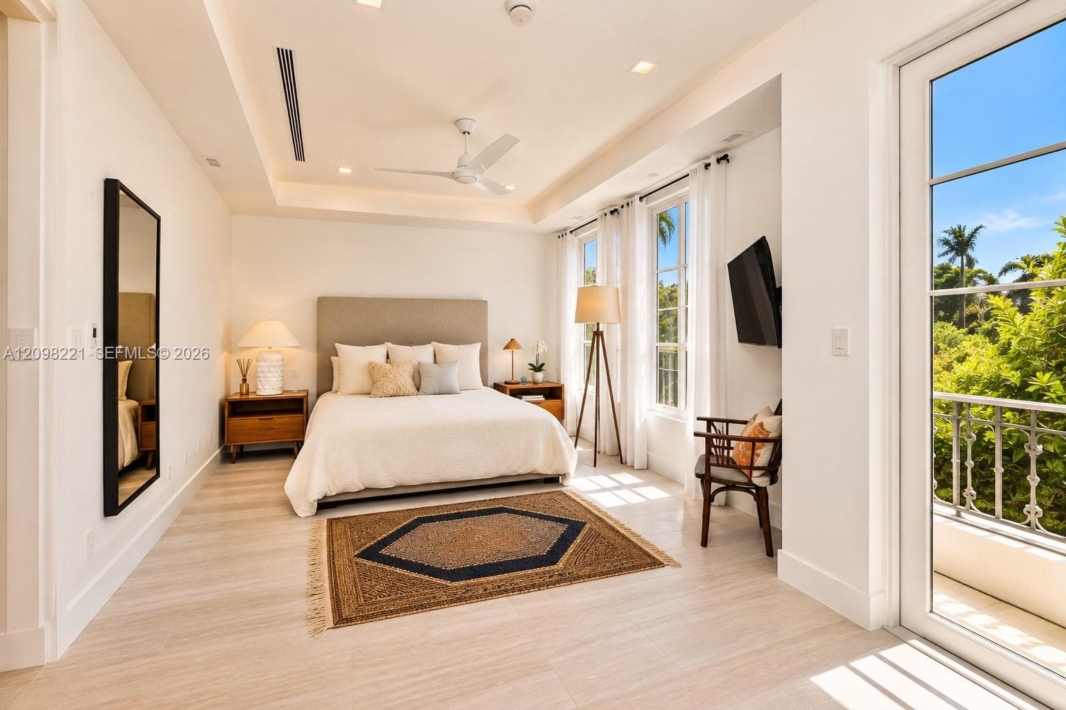 Tray ceiling featuring a central fan, wood-finish flooring, dual windows with natural light, and a door opening to a private balcony with ornate metal railing