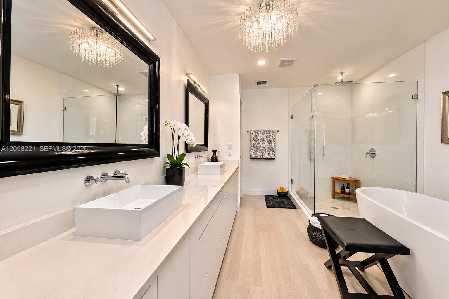 Long vanity with dual vessel sinks, quartz countertop, wall-mounted faucets, glass-enclosed shower, and freestanding soaking tub