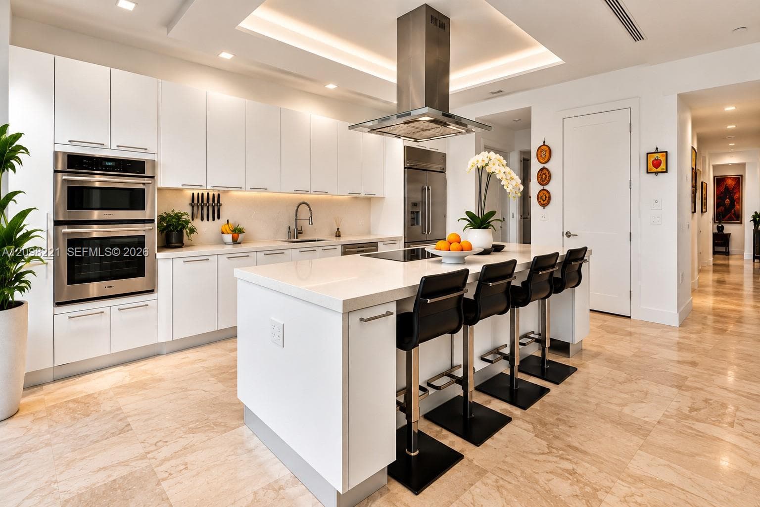 Gourmet kitchen featuring floor-to-ceiling cabinetry, a central island with a stone countertop, built-in stainless steel double wall ovens, a suspended stainless steel range hood, and tile flooring