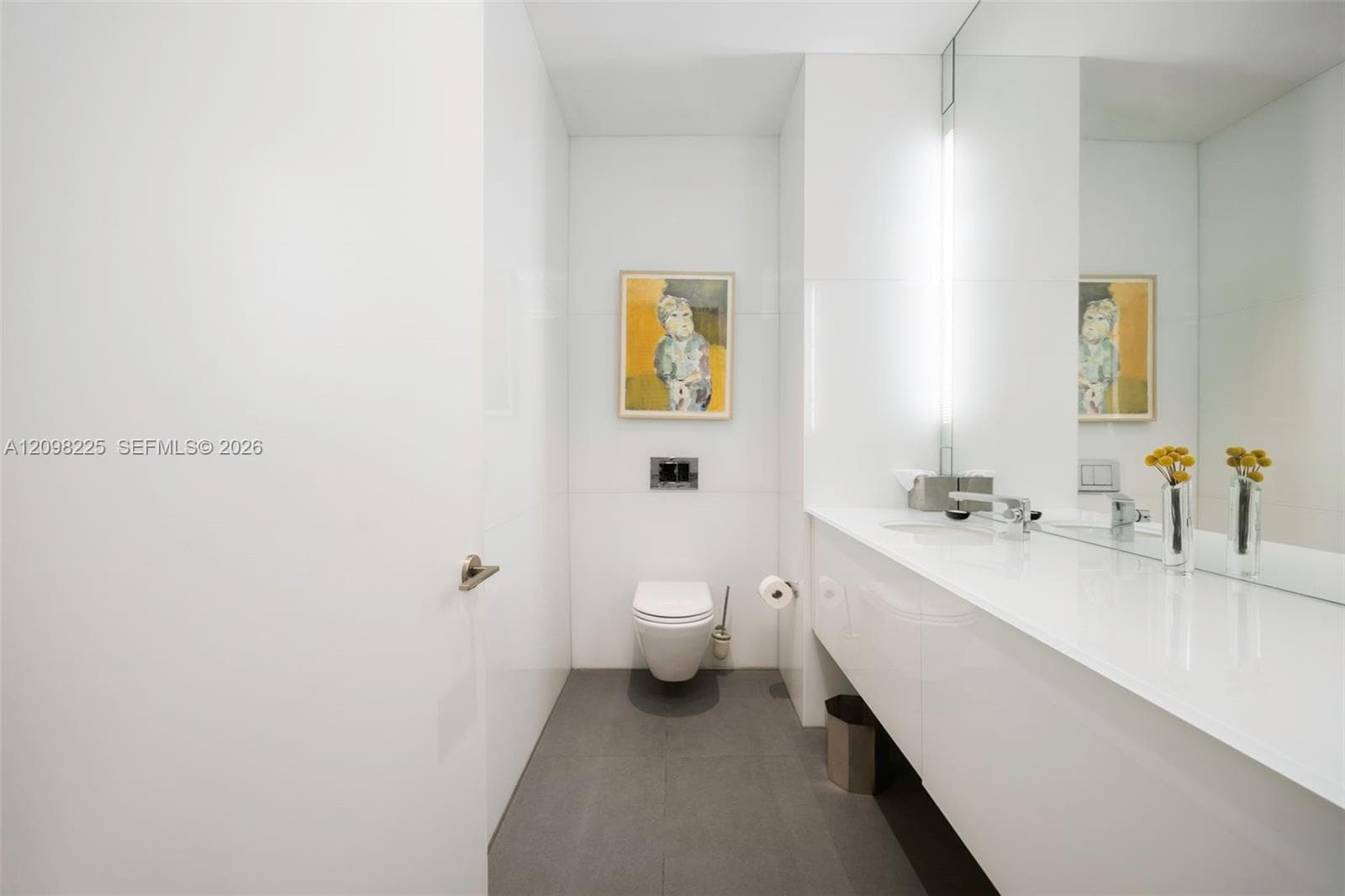 Wall-mounted toilet with a concealed tank, floating vanity with an integrated basin, large-format mirror, and matte-finish grey floor tile