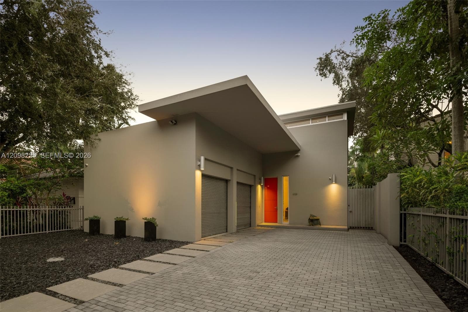 Modern architectural exterior featuring a prominent shed roofline, dual-car garage with roll-up doors, paver driveway, and a solid red entry door