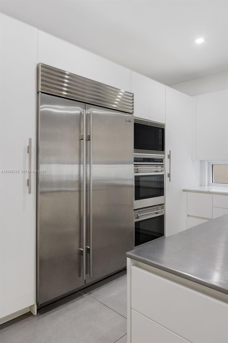 Kitchen featuring flat-panel white cabinetry, stainless steel built-in double-door refrigerator, integrated stainless steel double oven, stainless steel microwave, and metal countertop