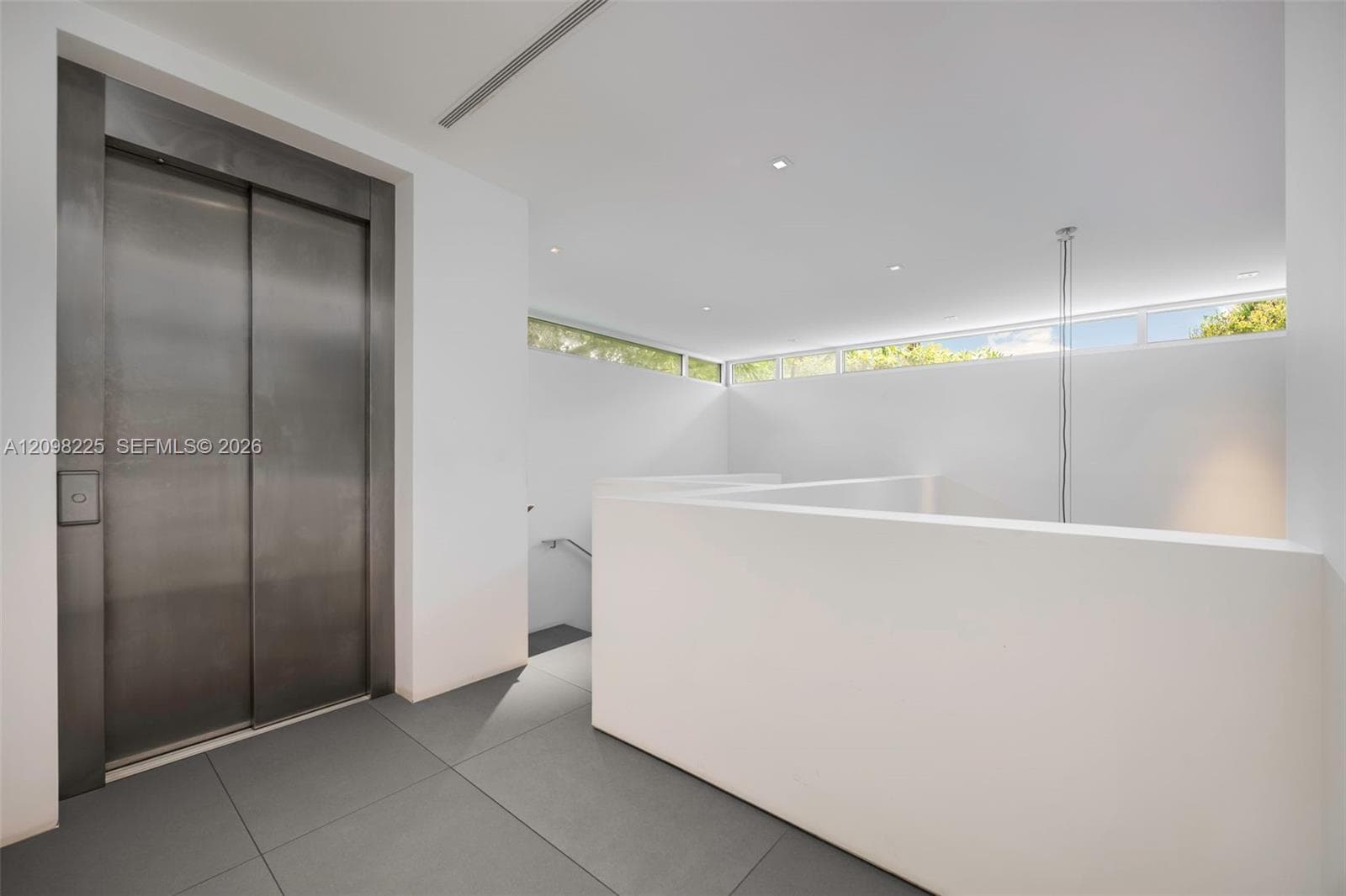 Stainless steel elevator, minimalist white walls, clerestory windows, recessed ceiling lighting, and large-format tile flooring