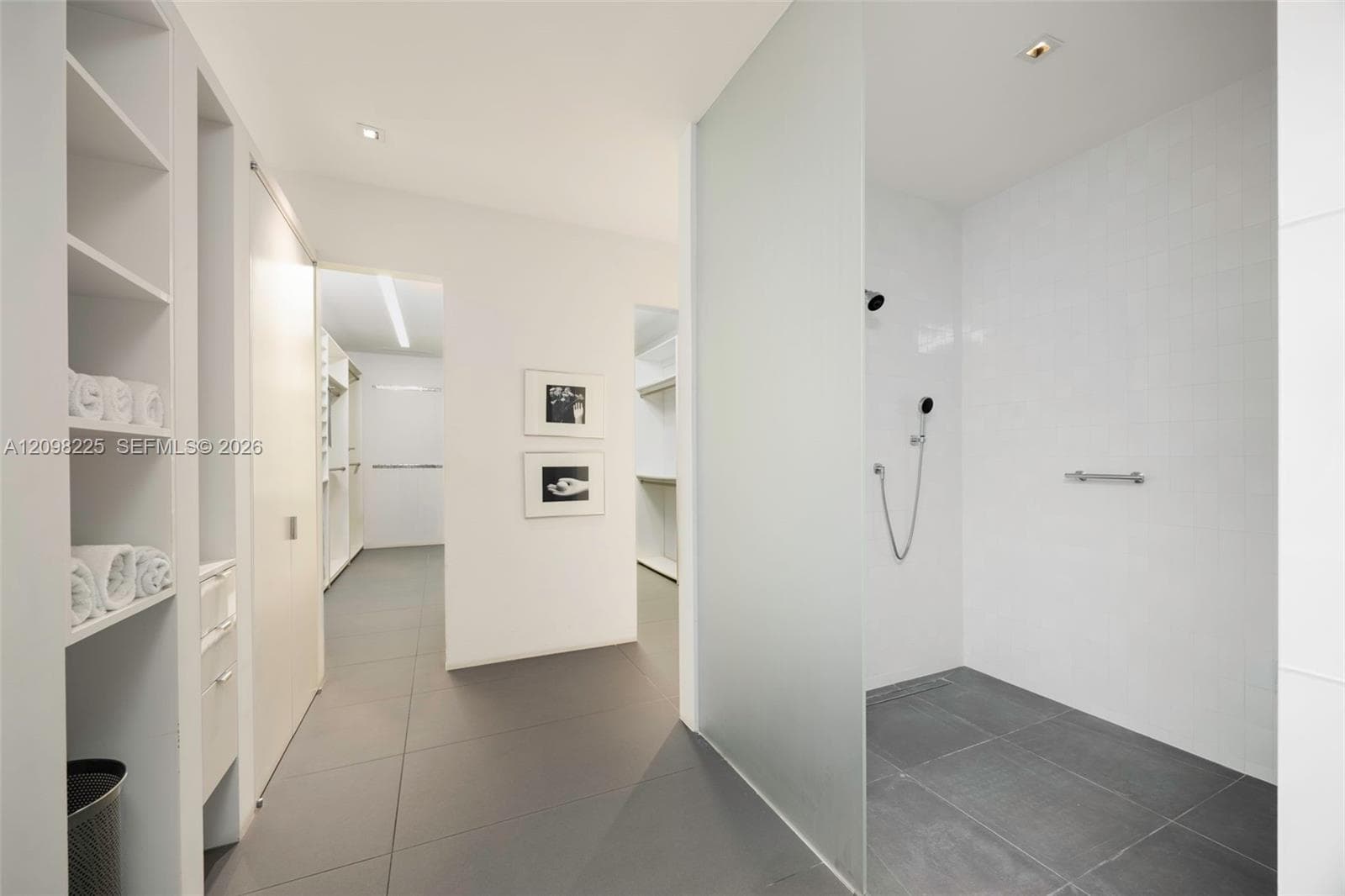 Walk-in shower featuring a frosted glass partition, chrome wall-mounted shower head, and large-format tile flooring, accompanied by built-in white shelving and cabinetry