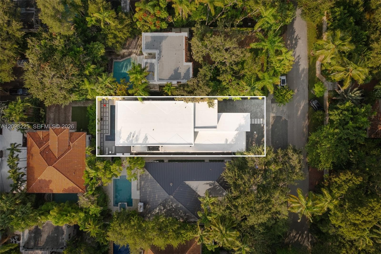 Aerial view of residential property featuring a linear swimming pool, paved hardscaping, and a rectangular multi-level roof structure situated within a mature tree canopy