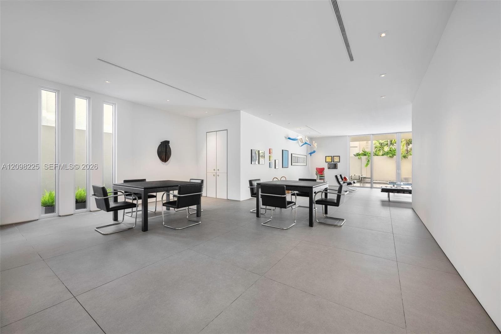 Expansive open-concept room featuring large-format tile flooring, recessed linear lighting, floor-to-ceiling windows, and glass sliding doors