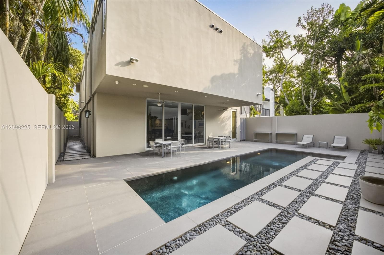 Modern exterior featuring a saltwater swimming pool, expansive concrete paver decking, decorative stone ground cover, and surrounding privacy walls