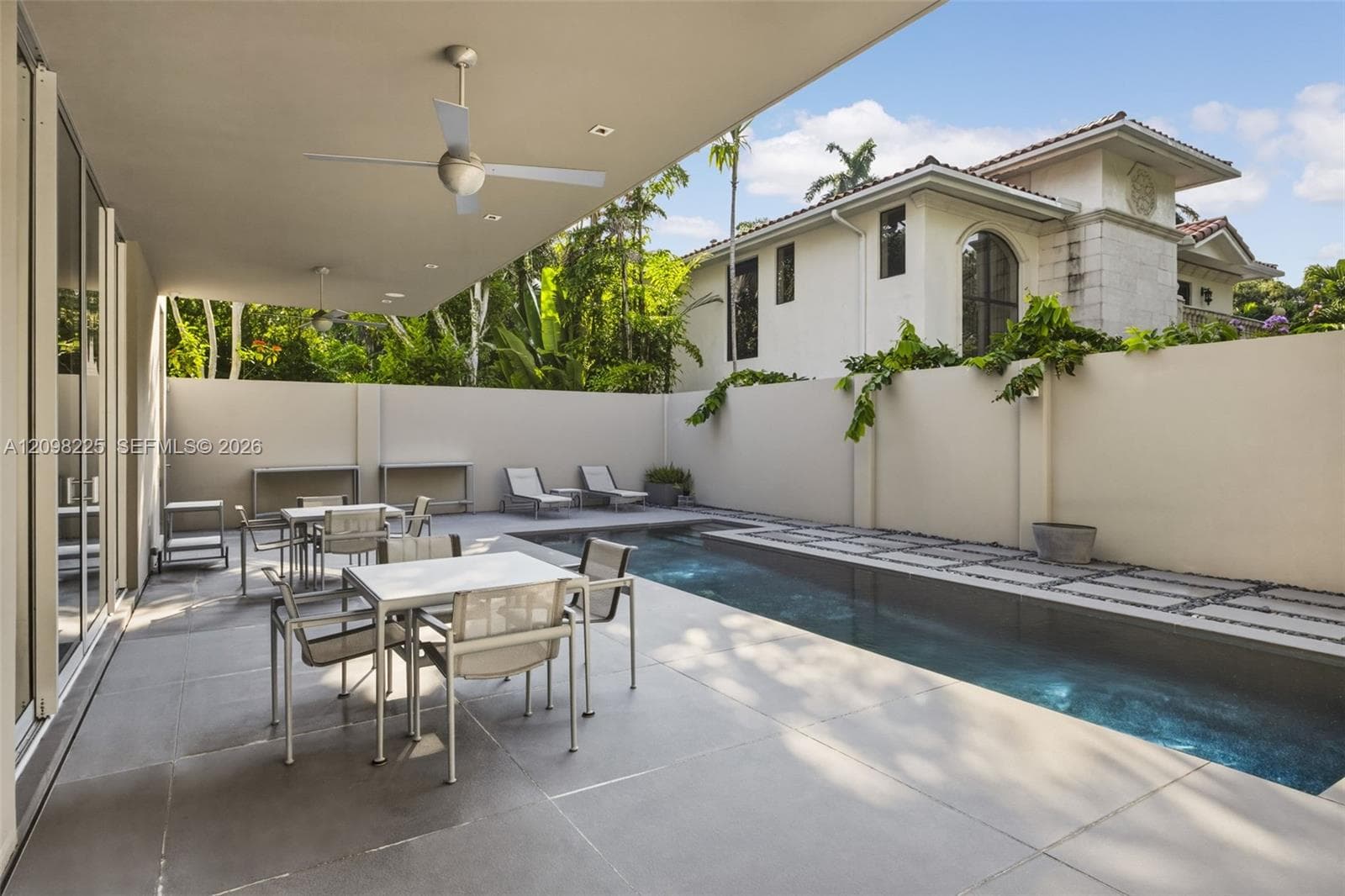 Covered outdoor patio featuring large-format concrete tile flooring and recessed ceiling fans, complemented by a private lap pool with stone pavers