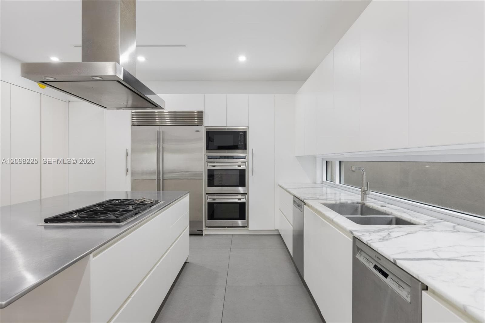Contemporary kitchen featuring flat-panel cabinetry, stainless steel island countertop with integrated cooktop, stone-surface perimeter countertops, stainless steel wall ovens, and recessed ceiling lighting