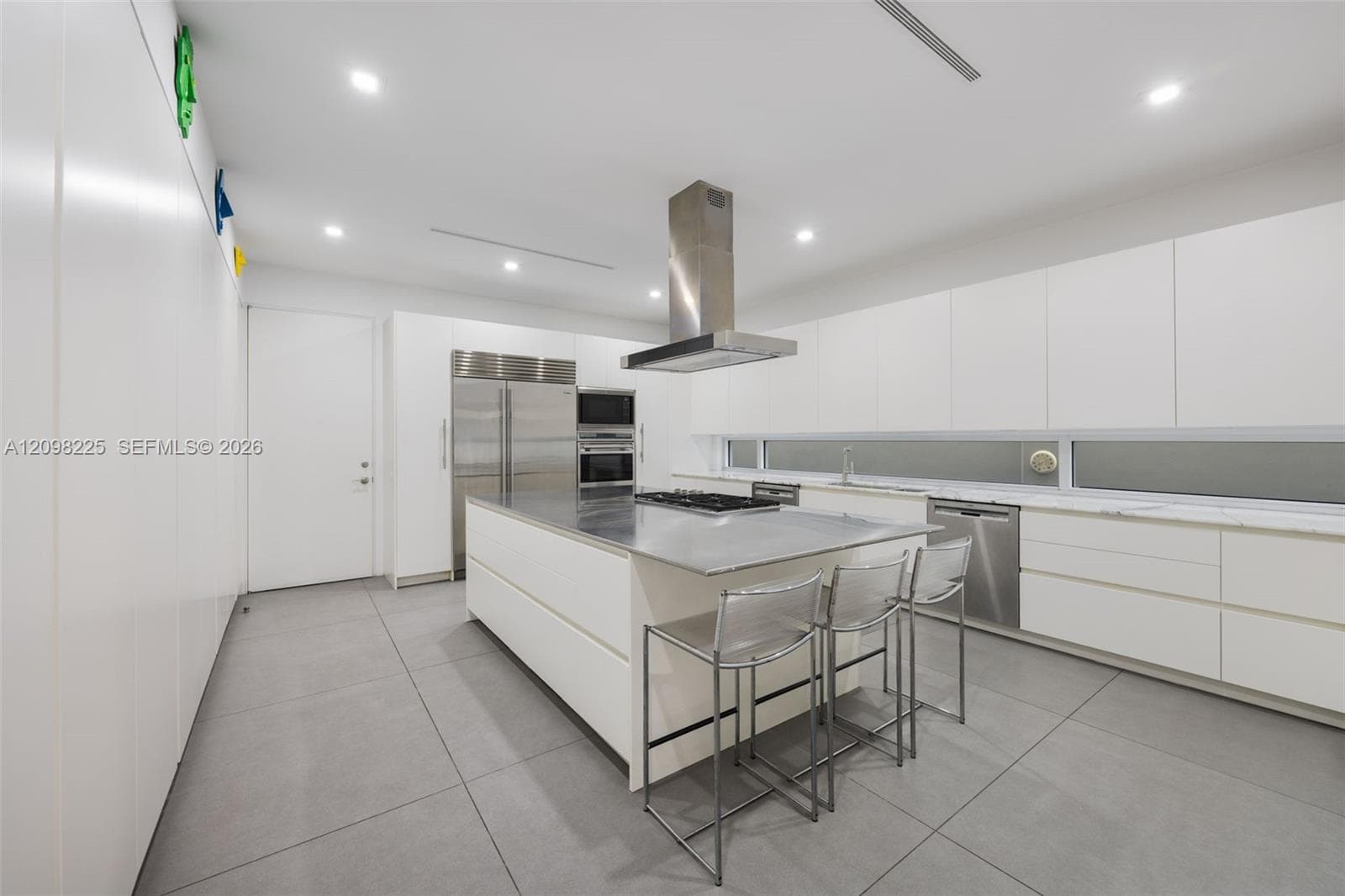 Contemporary kitchen featuring flat-panel cabinetry, a central island with a stainless steel countertop, professional-grade stainless steel appliances, a linear horizontal window, and large-format porcelain tile flooring