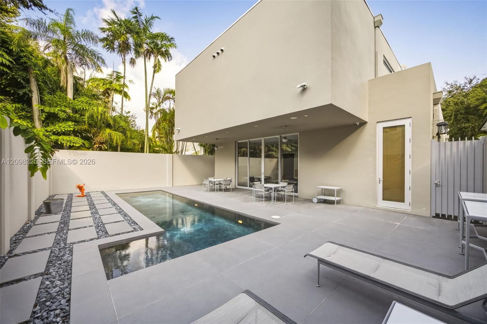 Modern stucco exterior featuring a swimming pool, concrete paver decking, decorative stone border, and privacy perimeter wall