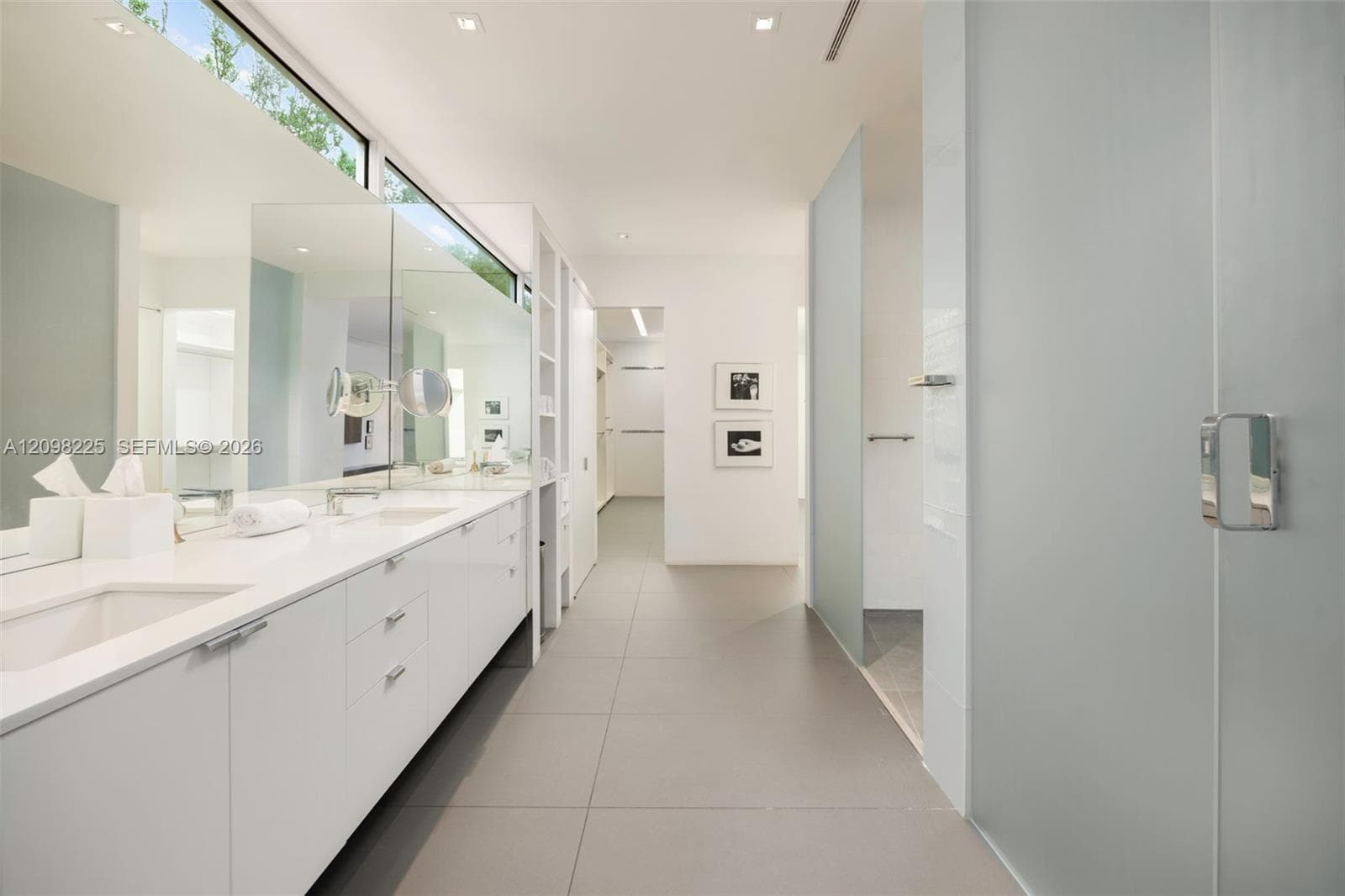 Dual vanity with white cabinetry, solid-surface countertop, full-width mirror, transom window, and tile flooring