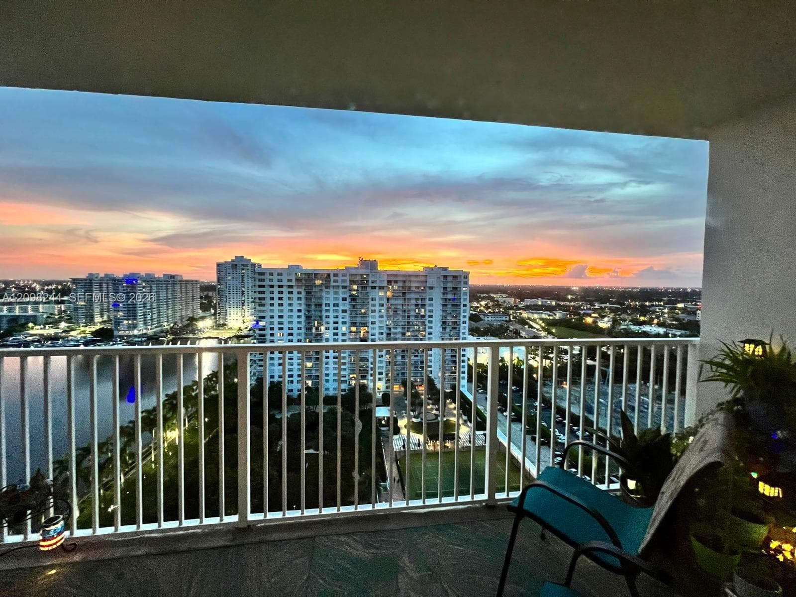 Covered balcony featuring white vertical railing, tile flooring, and water-front cityscape backdrop