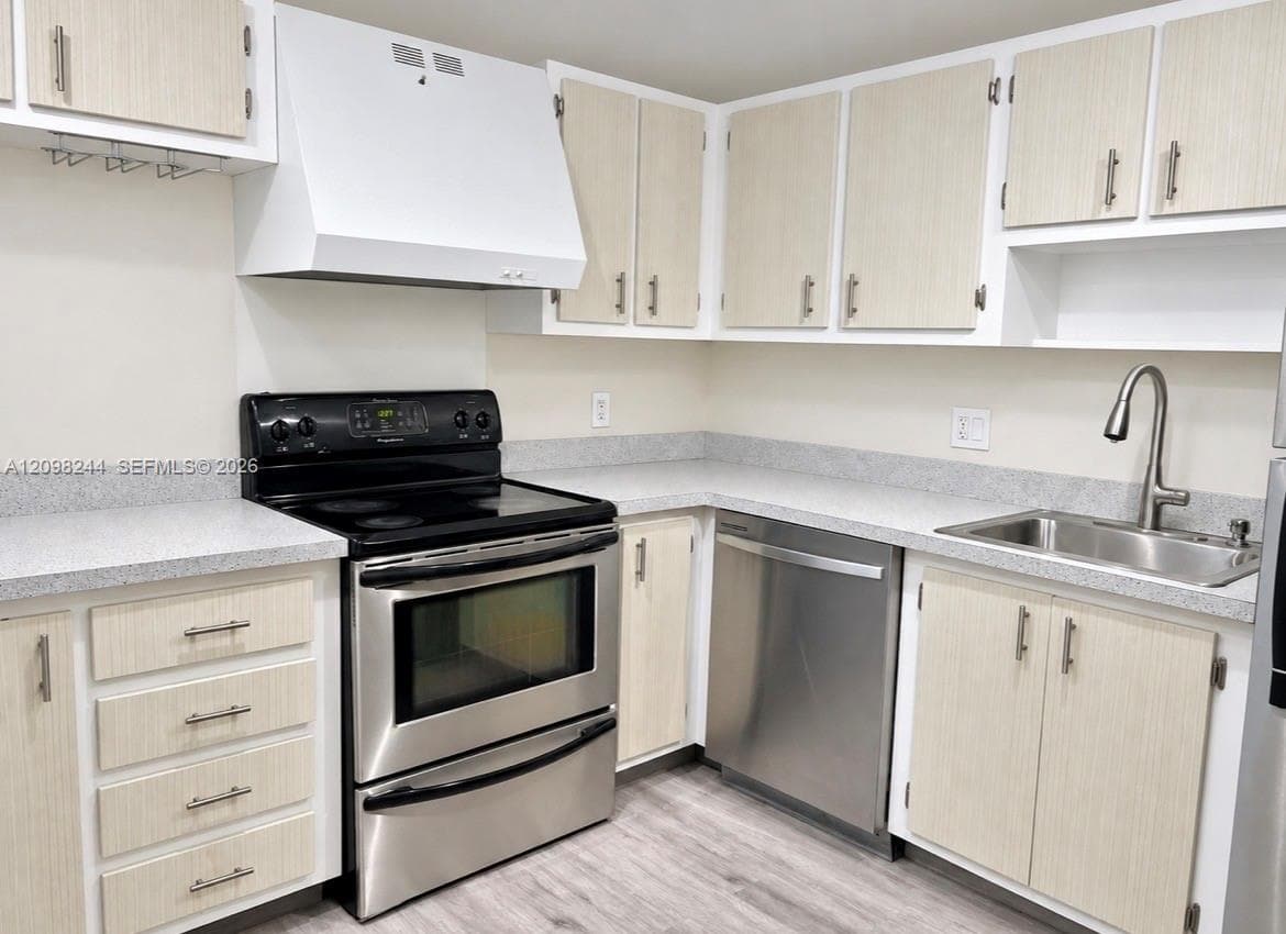 Kitchen featuring light-finish cabinetry, stainless steel appliances, speckled stone-composite countertops, stainless steel undermount sink with gooseneck faucet, and wood-finish flooring
